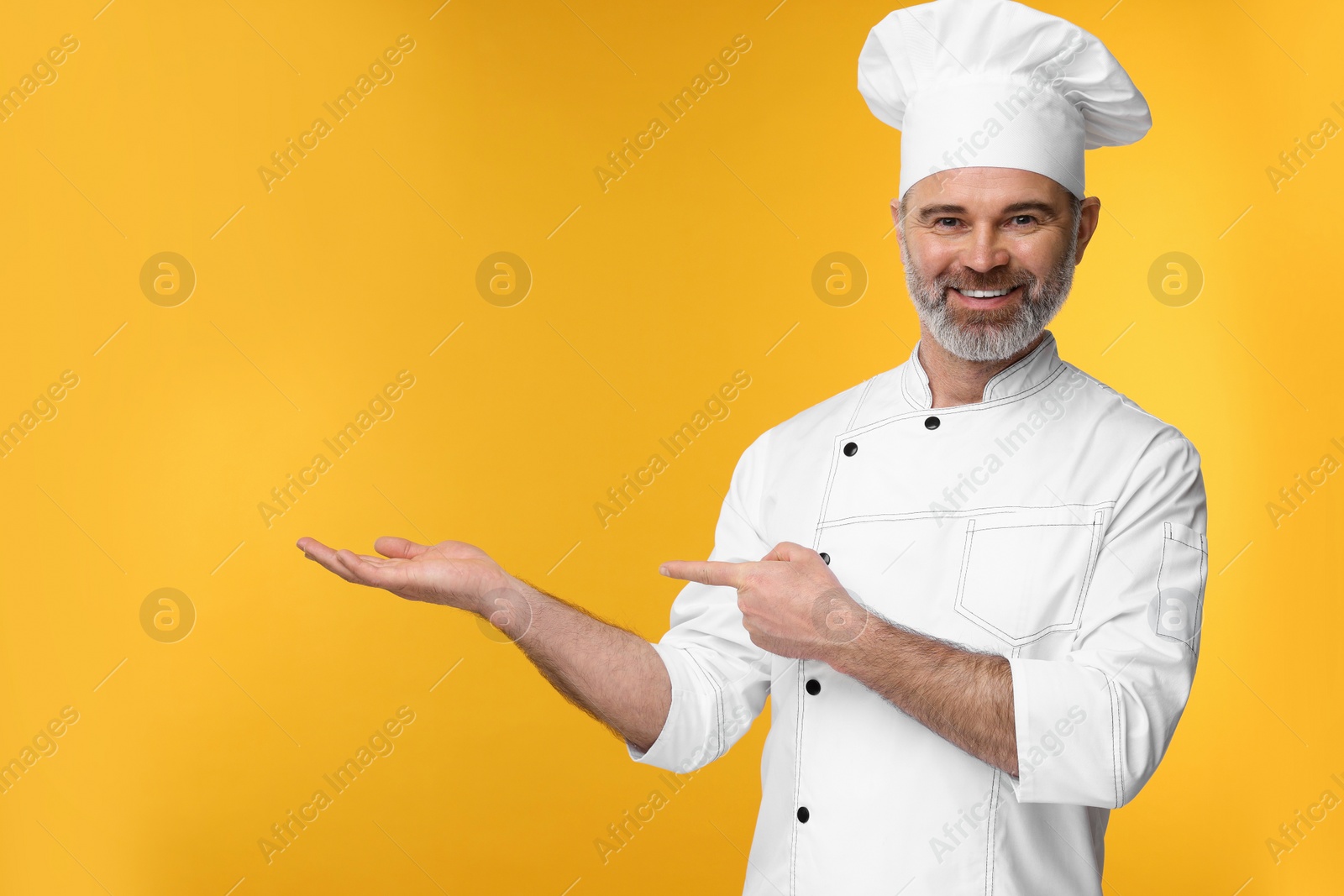 Photo of Happy chef in uniform showing something on orange background, space for text