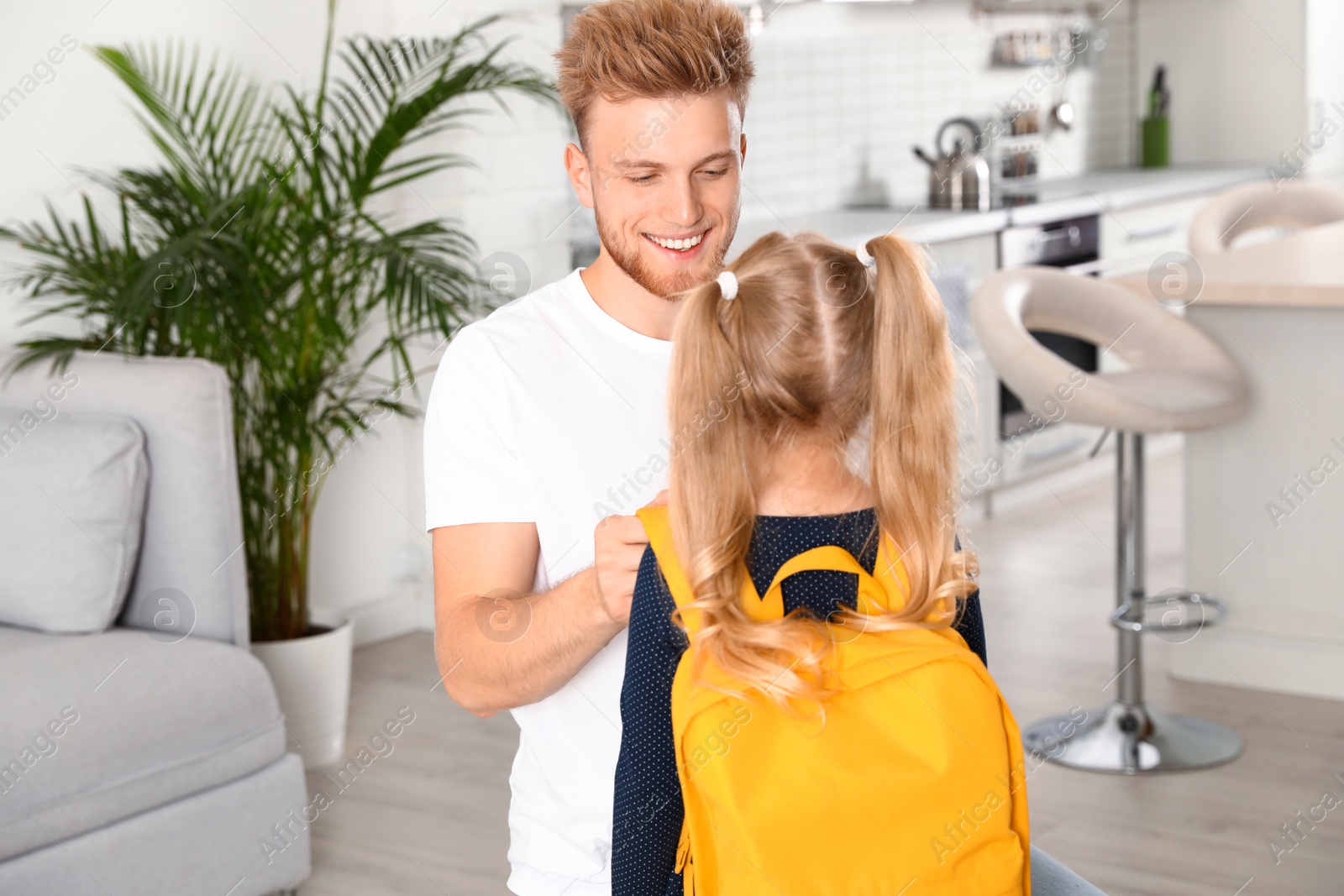 Photo of Happy father helping little child to put on school bag at home