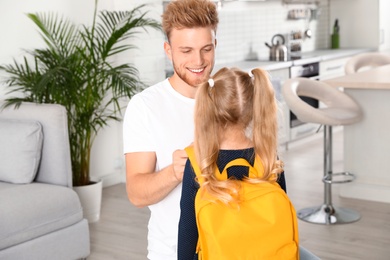 Photo of Happy father helping little child to put on school bag at home