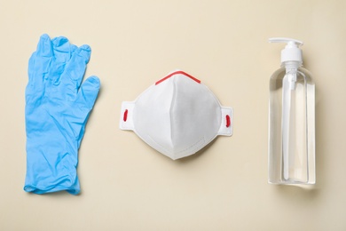 Photo of Medical gloves, respiratory mask and hand sanitizer on beige background, flat lay