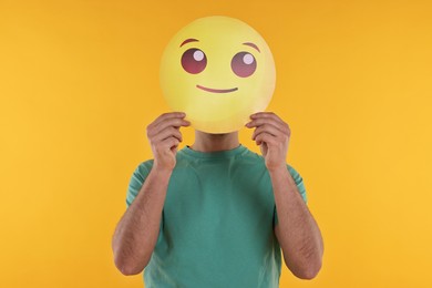 Photo of Man covering face with smiling emoticon on yellow background