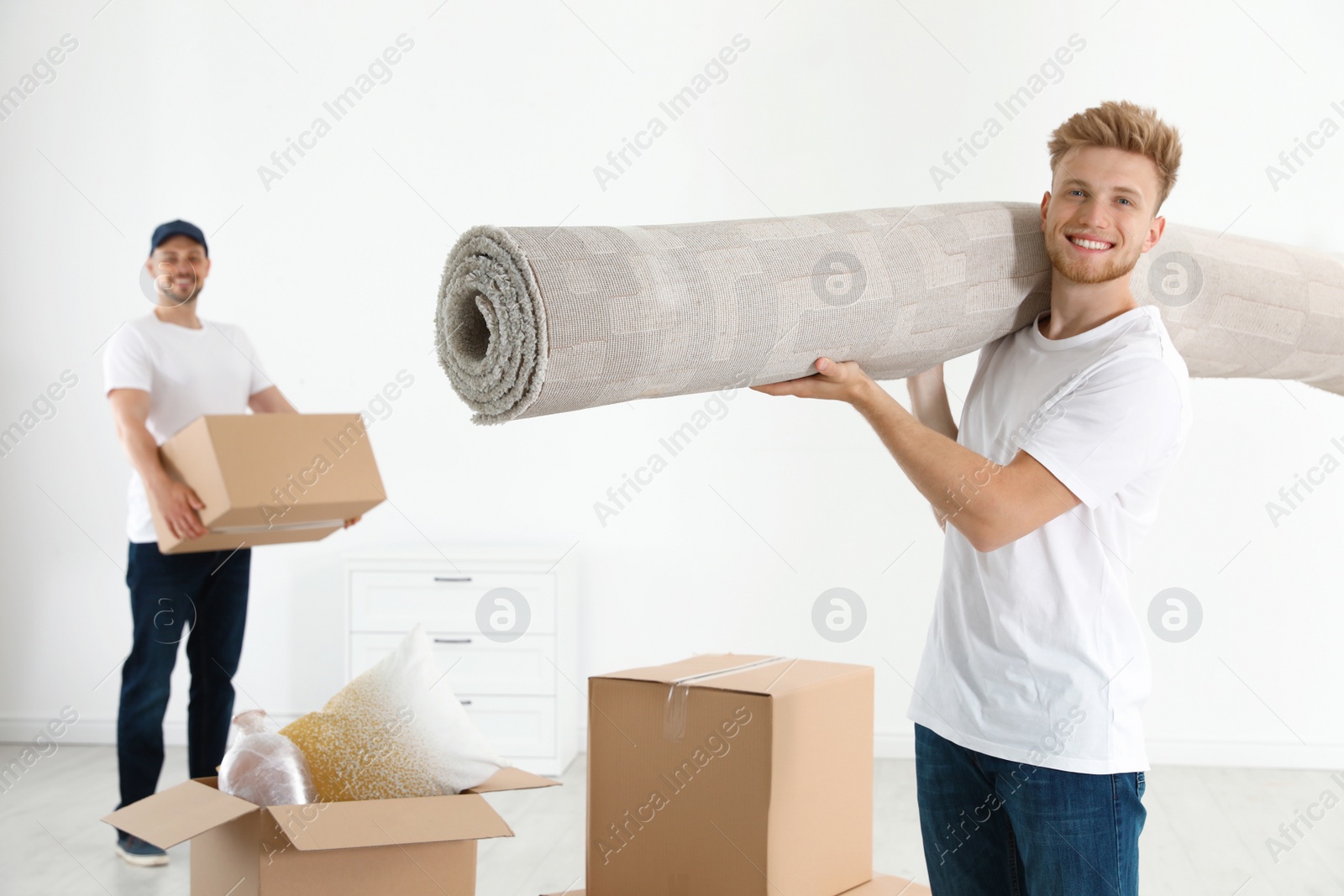 Photo of Moving service employees with cardboard boxes and carpet in room