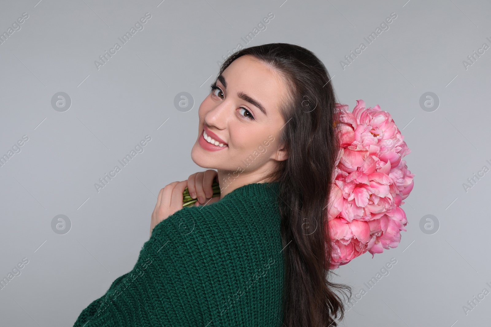 Photo of Beautiful young woman with bouquet of peonies on light grey background