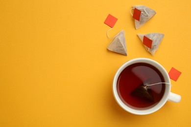 Photo of Tea bags and cup of hot drink on orange background, flat lay. Space for text