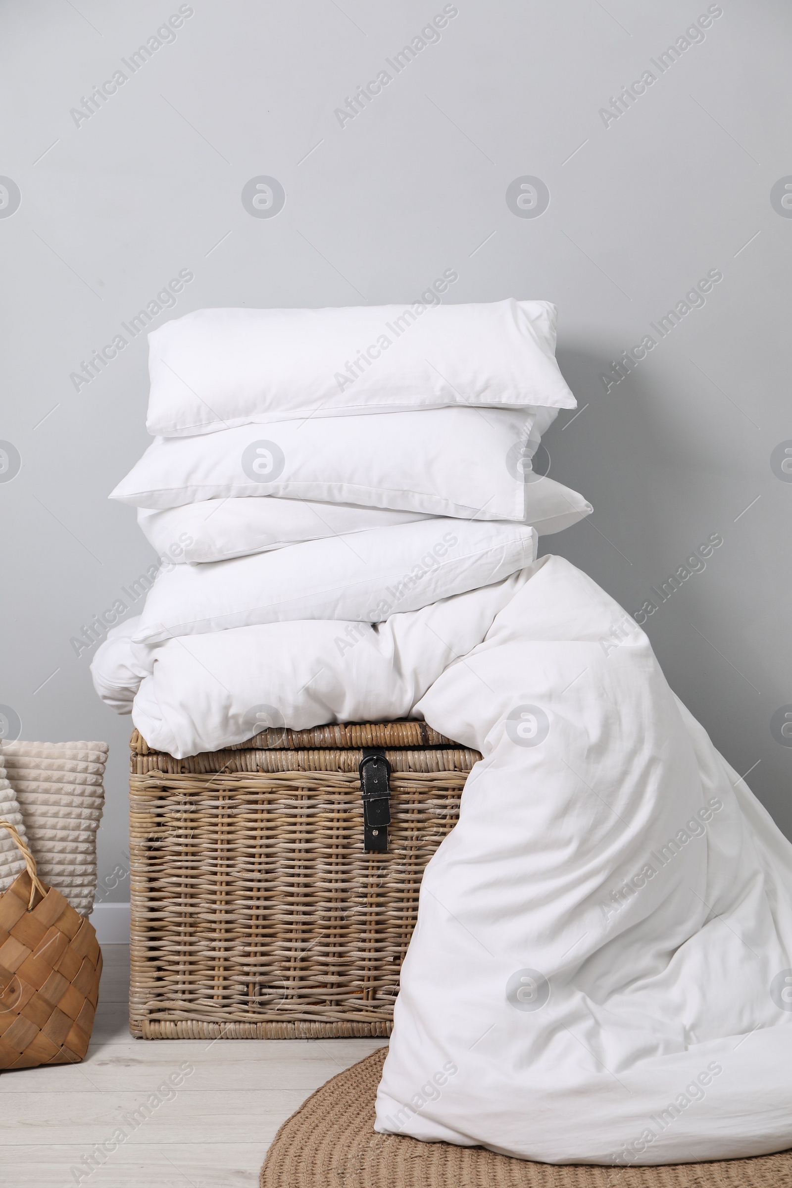 Photo of Soft pillows, duvet, bag and wicker trunk indoors