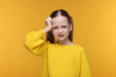 Little girl suffering from headache on yellow background