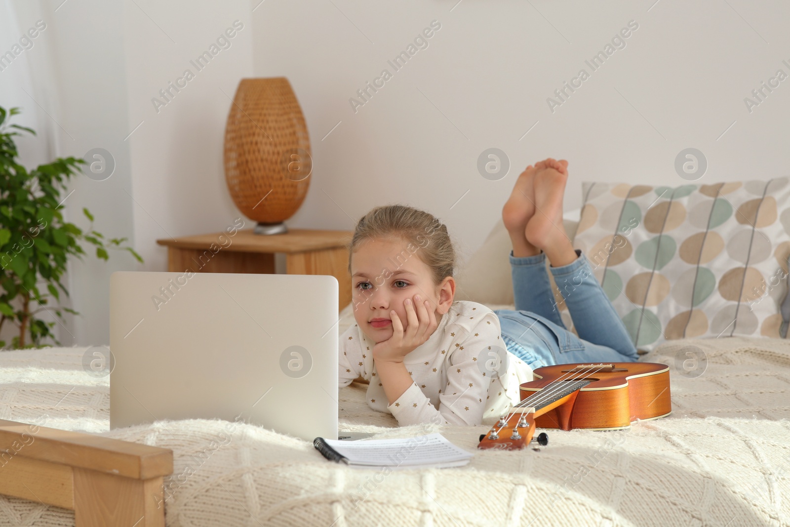 Photo of Little girl learning to play ukulele with online music course at home. Time for hobby