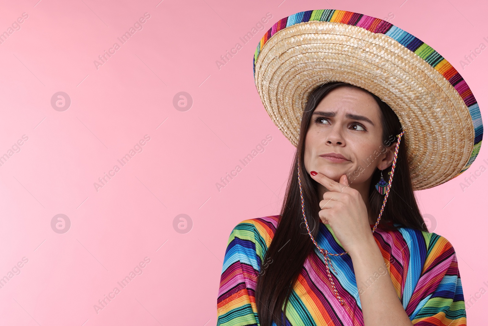 Photo of Thoughtful woman in Mexican sombrero hat and poncho on pink background. Space for text