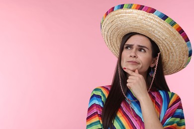 Photo of Thoughtful woman in Mexican sombrero hat and poncho on pink background. Space for text