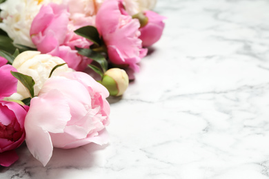 Photo of Beautiful peonies on white marble background, closeup. Space for text