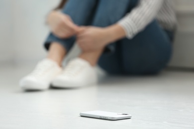 Photo of Lonely woman sitting on floor and smartphone on foreground, closeup