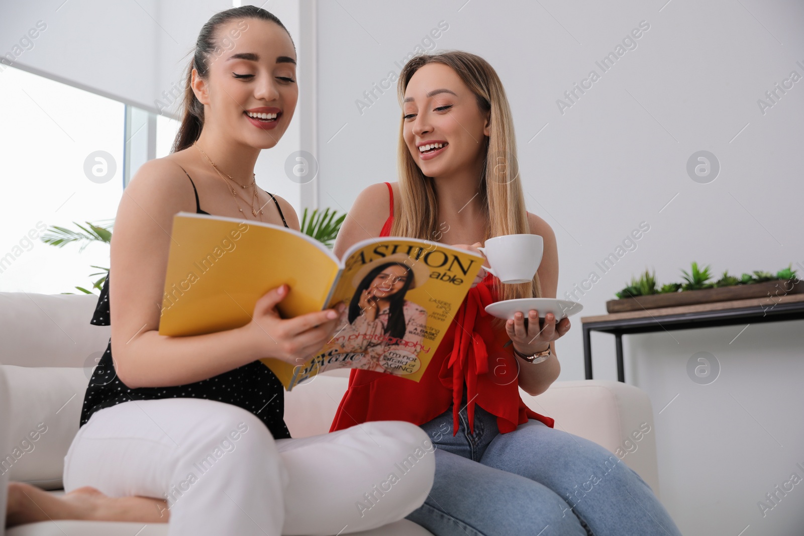 Photo of Happy women reading magazine on sofa in room