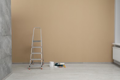 Photo of Metallic folding ladder and painting tools near beige wall indoors, space for text