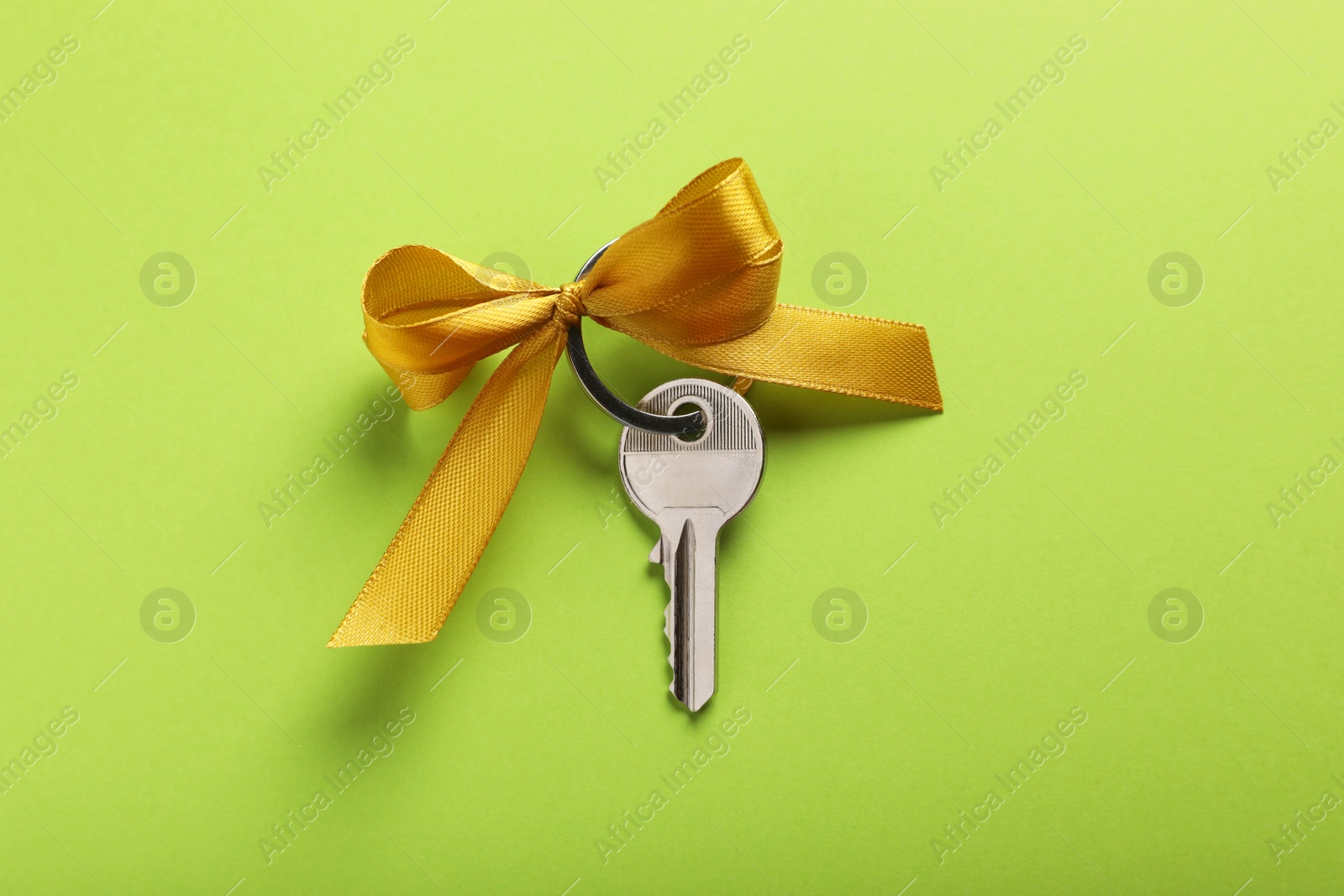 Photo of Key with yellow bow on light green background, top view. Housewarming party