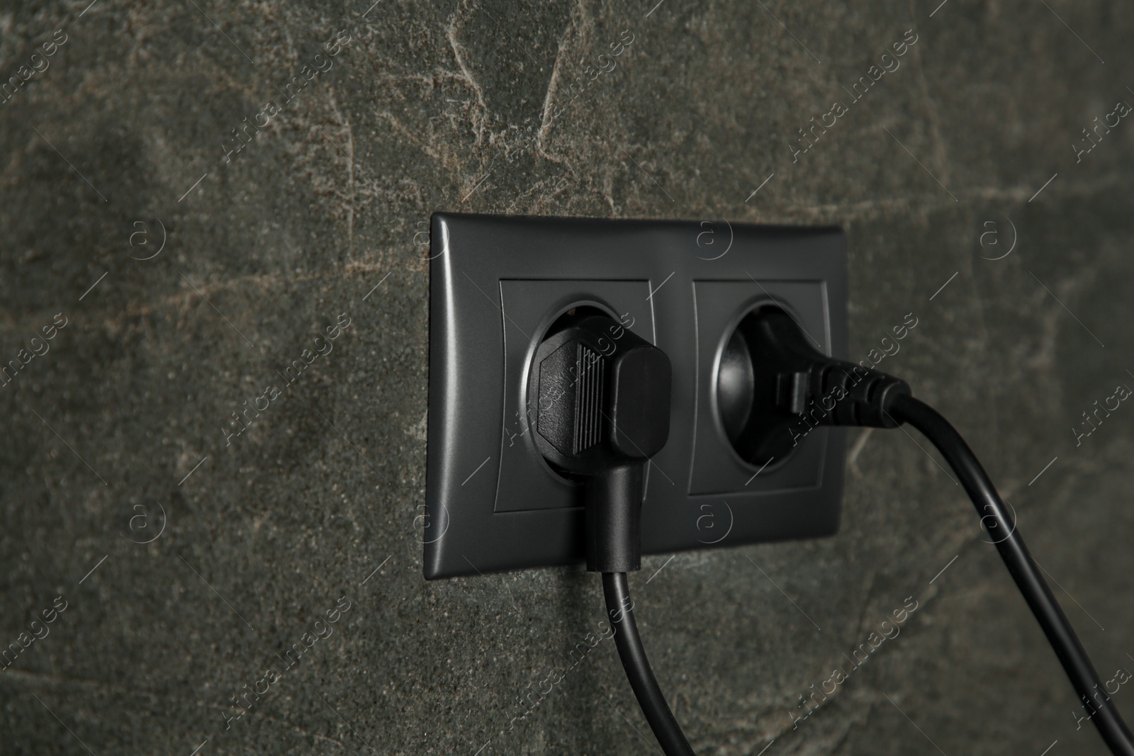 Photo of Power sockets with inserted plugs on dark grey wall, closeup. Electrical supply