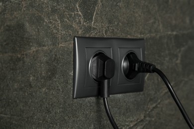 Photo of Power sockets with inserted plugs on dark grey wall, closeup. Electrical supply