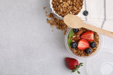 Photo of Tasty granola with berries and nuts in plastic cup on light table, top view. Space for text