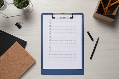 Photo of Clipboard with checkboxes, plant and office stationery on white wooden table, flat lay. Checklist