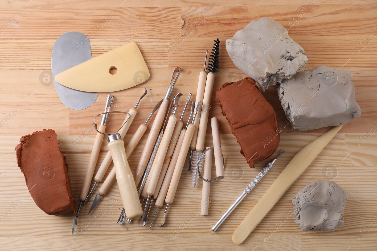 Photo of Clay and set of modeling tools on wooden table, flat lay