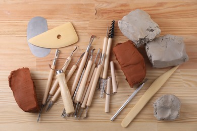 Clay and set of modeling tools on wooden table, flat lay