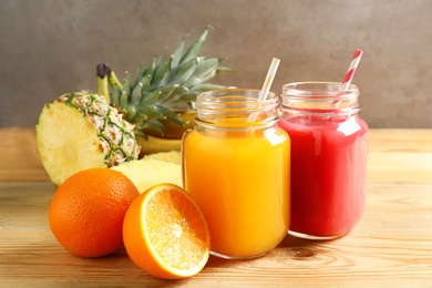 Photo of Mason jars with different juices and fresh fruits on wooden table against color background