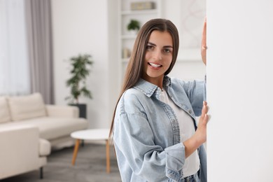 Photo of Happy woman standing near white wall at home, space for text. Invitation to come in room
