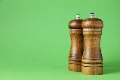 Photo of Wooden salt and pepper shakers on green background, closeup. Space for text