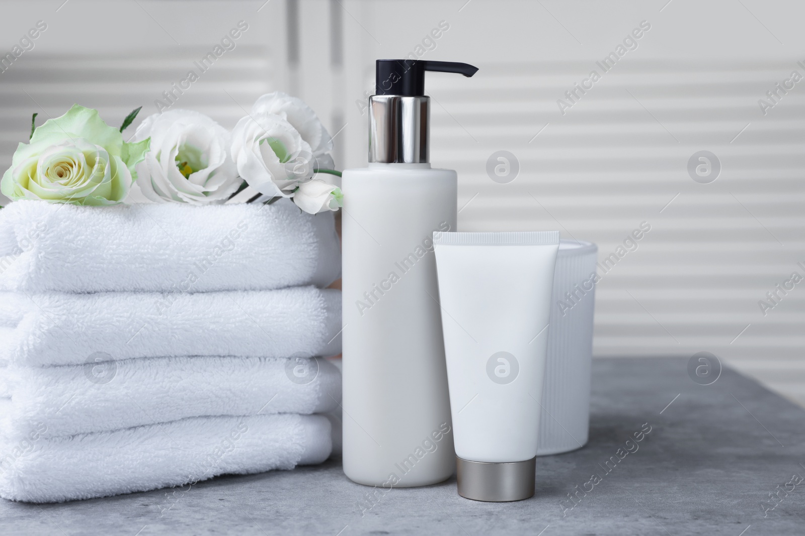 Photo of Towels, cosmetic products and flowers on grey table indoors