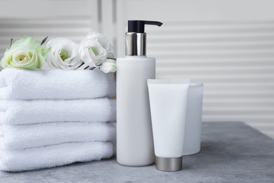 Towels, cosmetic products and flowers on grey table indoors