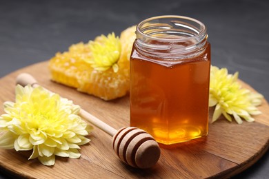 Sweet honey in jar, dipper and chrysanthemum flowers on grey table
