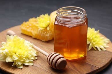 Photo of Sweet honey in jar, dipper and chrysanthemum flowers on grey table