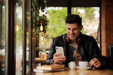 Man with headphones and smartphone at table in cafe
