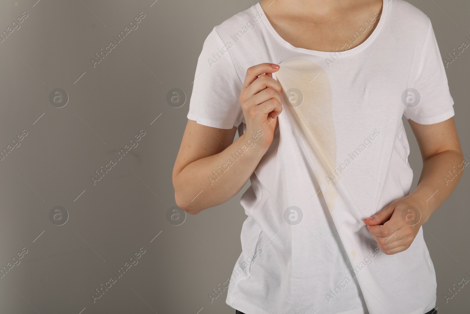 Photo of Woman showing stain from coffee on her shirt against light grey background, closeup. Space for text
