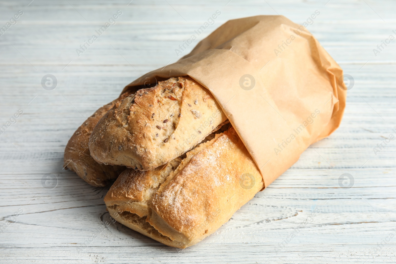 Photo of Mini baguettes in paper bag on wooden table, closeup. Wholegrain bread