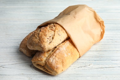 Photo of Mini baguettes in paper bag on wooden table, closeup. Wholegrain bread