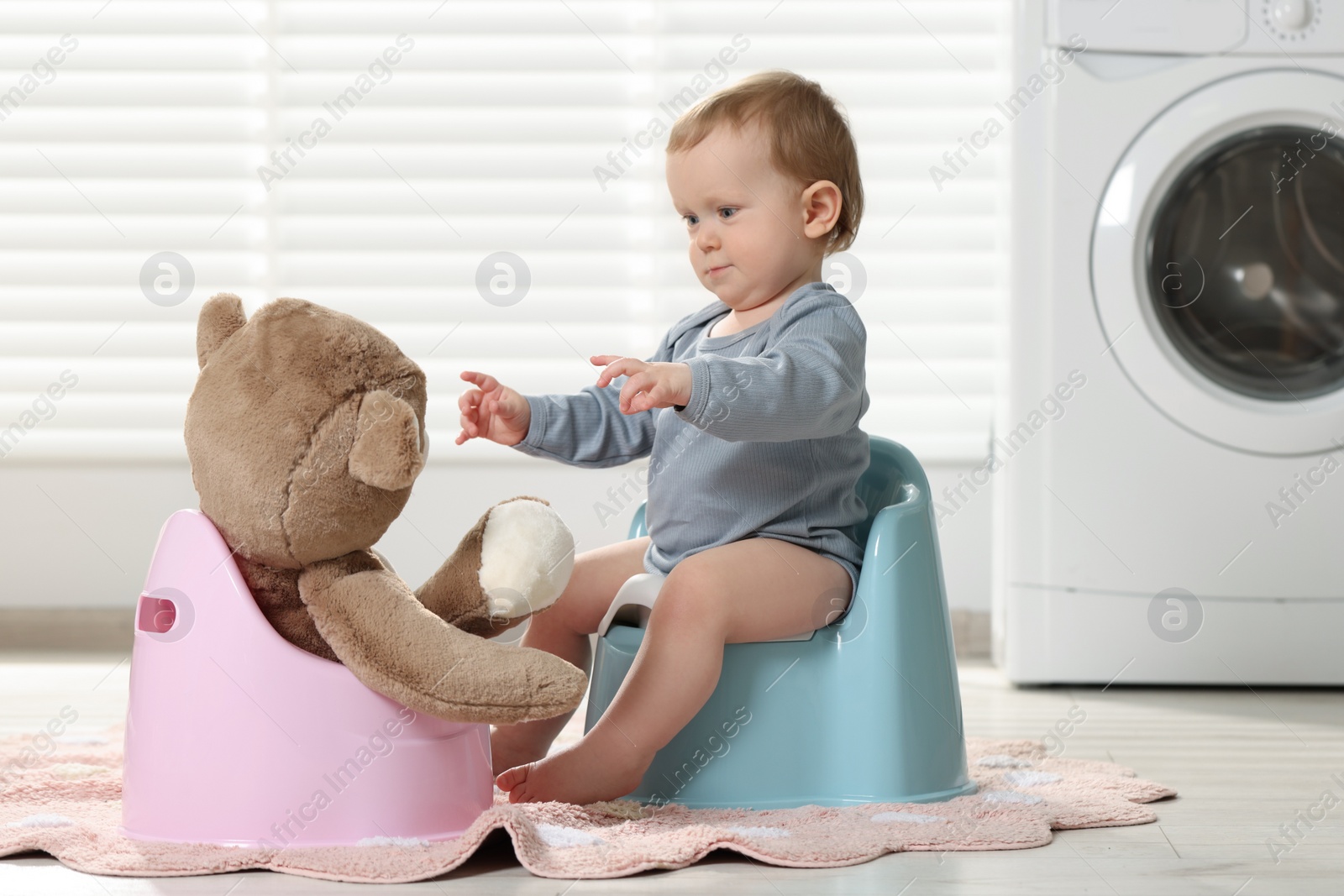 Photo of Little child and teddy bear sitting on plastic baby potties indoors