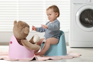 Little child and teddy bear sitting on plastic baby potties indoors