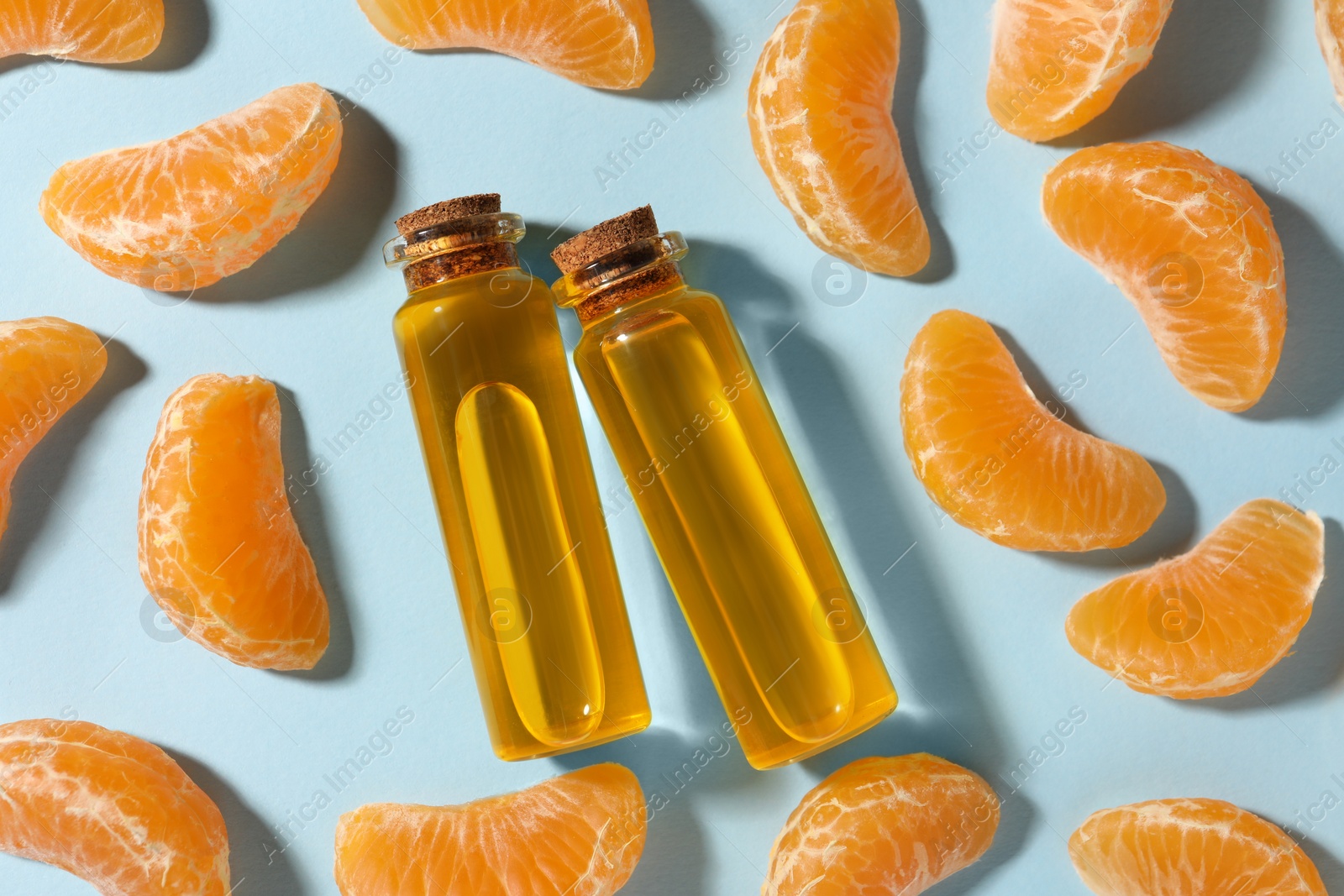 Photo of Aromatic tangerine essential oil in bottles and citrus fruits on light blue table, flat lay