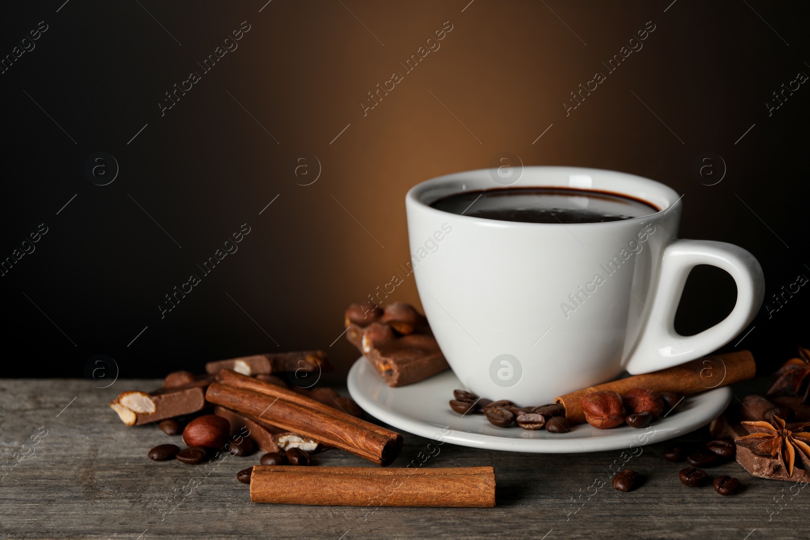 Photo of Cup of delicious hot chocolate, spices and coffee beans on wooden table. Space for text