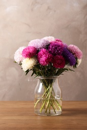 Vase with beautiful aster flower bouquet on table against color background