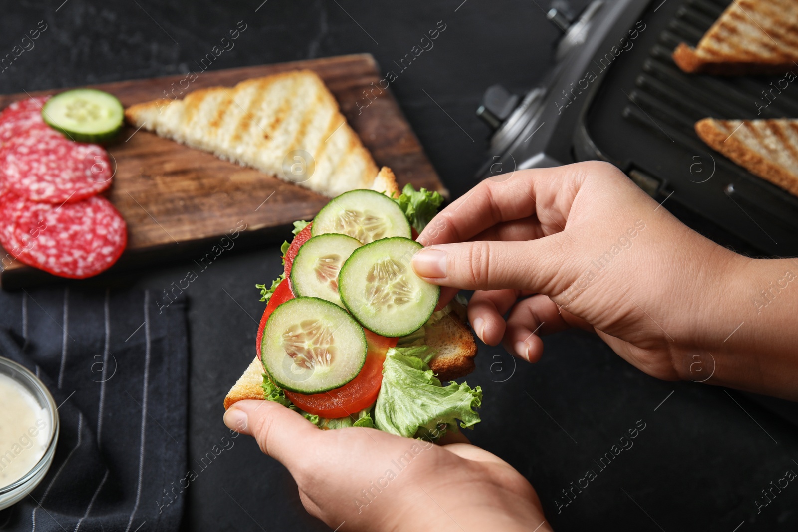 Photo of Woman adding cucumber to sandwich at black table, closeup