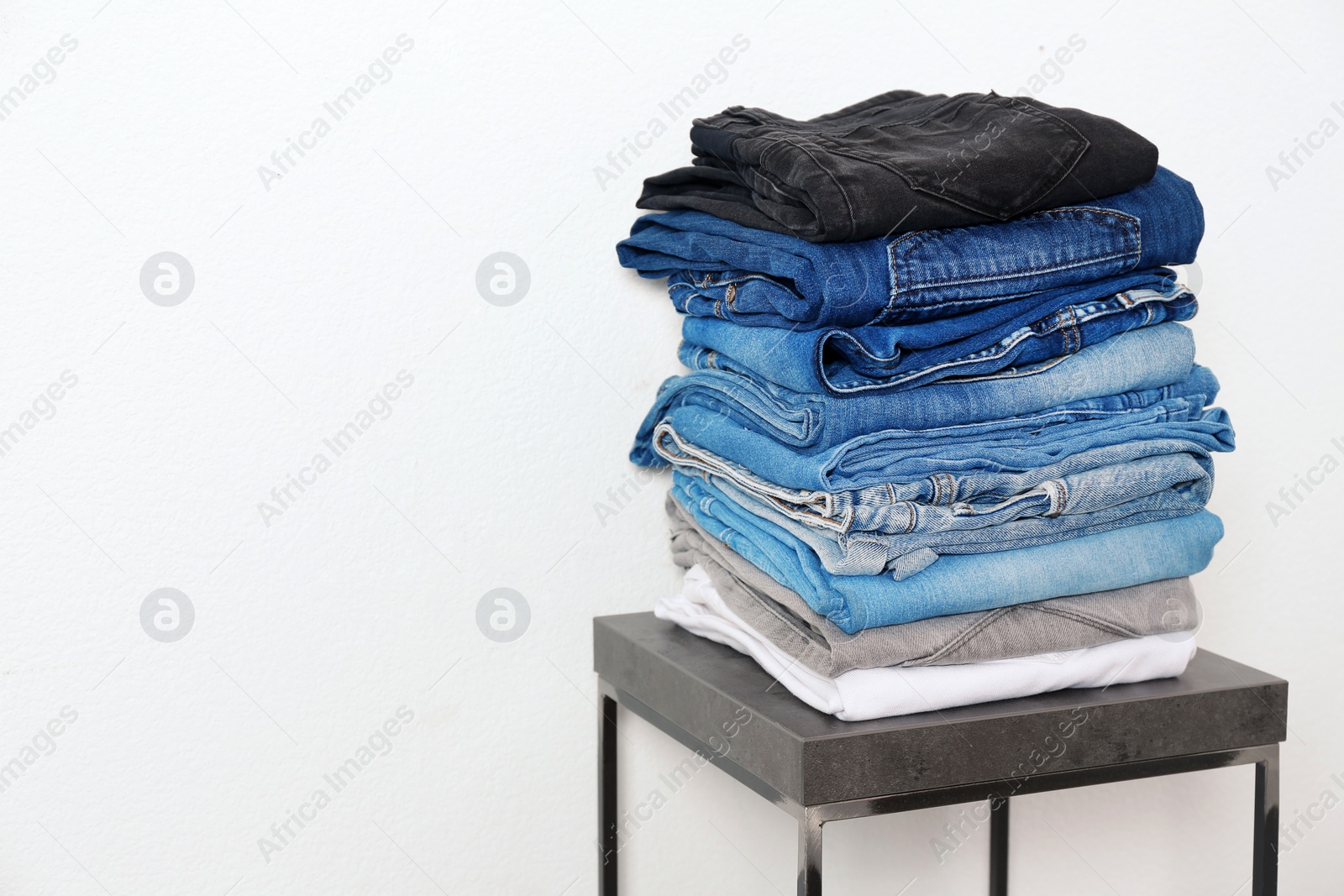 Photo of Stack of different jeans on table against white background. Space for text