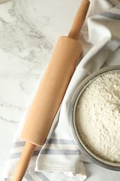 Photo of Flour in bowl, rolling pin and napkin on white marble table, top view