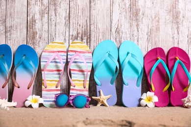 Different bright flip flops and sunglasses on sand near wooden wall, space for text. Summer beach accessories