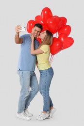 Photo of Lovely couple with heart shaped balloons taking selfie on light grey background. Valentine's day celebration