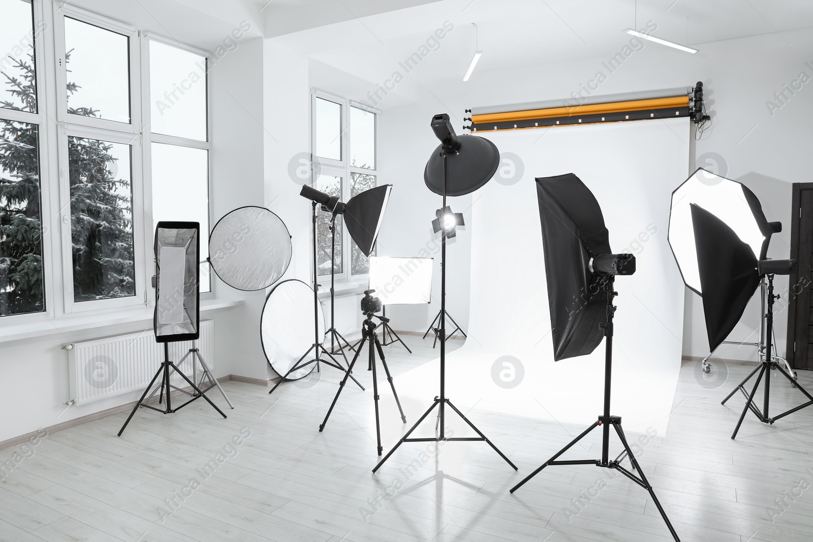 Photo of Tripod with camera and professional lighting equipment in modern photo studio