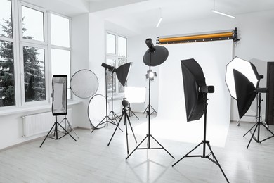 Photo of Tripod with camera and professional lighting equipment in modern photo studio
