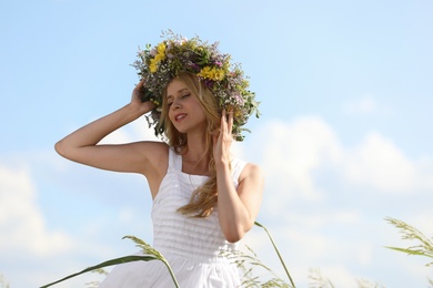 Young woman wearing wreath made of beautiful flowers outdoors on sunny day