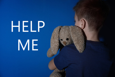 Scared little boy with bunny and text HELP ME on blue background