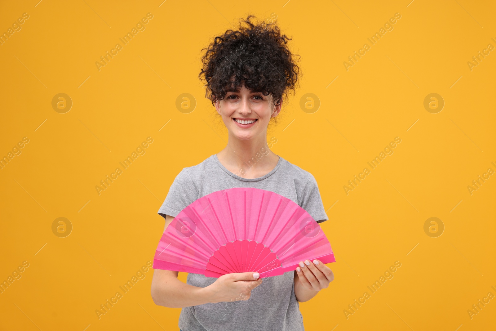 Photo of Happy woman holding hand fan on orange background